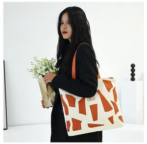 Close-up of cream canvas tote bag with orange geometric patterns and textile shoulder strap