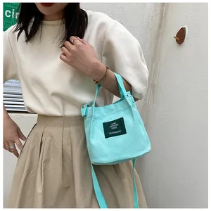 Detail of mint green canvas messenger bag with black rectangular label and shoulder strap