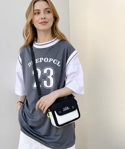Side view of a casual black and white canvas crossbody bag worn by a model in a grey T-shirt