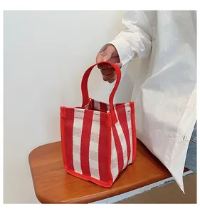 Détail du petit sac cabas en toile rayé rouge et blanc tenu à la main sur un banc