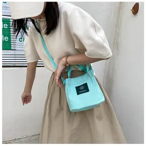 Detailed close-up of mint green canvas bucket bag featuring a black text label and long strap