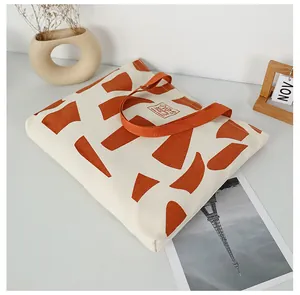 Detail of canvas tote bag showing orange woven handles and geometric pattern accents