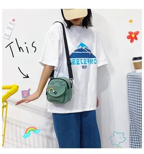 Close-up of a light green canvas crossbody bag with rainbow badge and adjustable strap