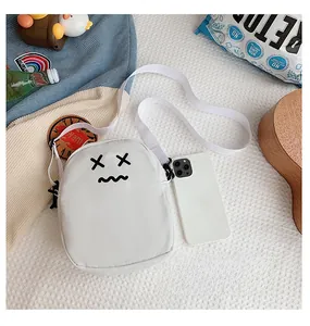 Mini white crossbody bag with cartoon face shown next to a smartphone for size scale