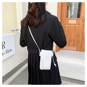 Buitenfoto van een minimalistische witte crossbody mini-telefoontas met knoopdetail