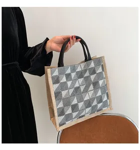 Detail of grey and white checkered canvas tote bag with black handles in daily hand-held use