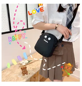 Close-up of black canvas crossbody bag with white monster expression and nylon strap