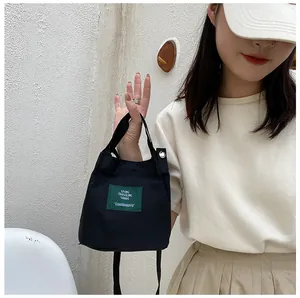 Detailed view of a black mini canvas tote bag with a green woven label and shoulder strap
