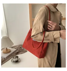 Detail shot of red corduroy tote bag showing ribbed texture and metal ring on shoulder strap