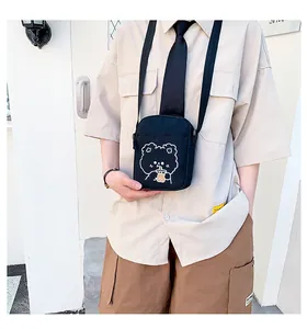 Detalle de un bolso bandolera de lona negra con estampado de un oso bebiendo té de leche
