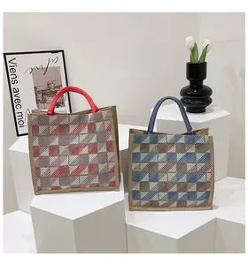Detail view of woven jute tote bags with red and blue handles on a minimalist pedestal