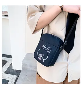 Detalle de bolso bandolera de lona negra con bordado de conejo blanco y correa ajustable
