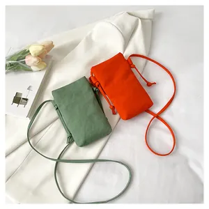 Detailopname van mini canvas crossbodytassen in groen en oranje op een witte blazer