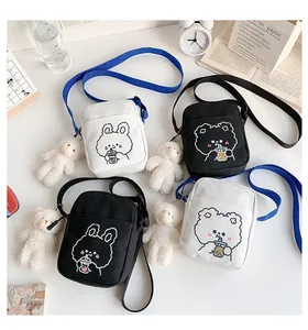 Detalle de bolsos bandolera de lona con bordado de oso y accesorio de peluche suave