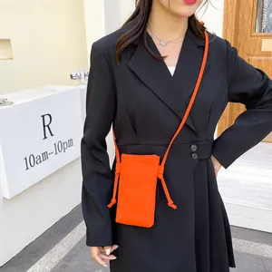 Mini oranje canvas crossbody telefoontas voor dames gedragen door een model in blazer