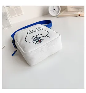Detalle de bolso bandolera de lona blanca con estampado de oso azul y correa de nailon azul