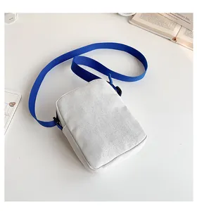 Detalle de un pequeño bolso bandolera de lona blanca con correa azul y diseño ajustable