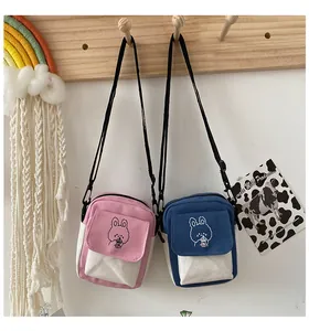 Detail of pink and blue canvas mini crossbody bags with cartoon rabbit on a wooden rack