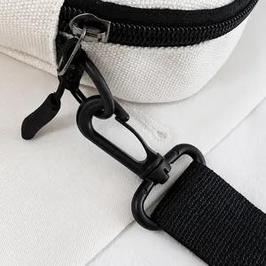 Detail view of durable black metal zipper and plastic hook on cream canvas shoulder bag