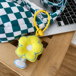 Detailansicht eines gelben Stoffanhängers in Blumenform an einer grün karierten Tasche