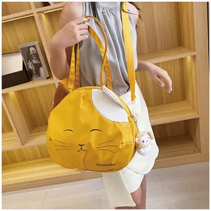 Detail of yellow cat-shaped canvas tote bag with plush sheep charm on a bookshelf