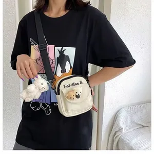 Detail of cream canvas crossbody bag featuring adjustable strap and cute plush bear charms