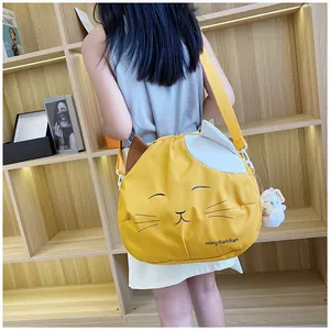 Detail of yellow cat-shaped canvas bag with plush pendant and adjustable shoulder strap