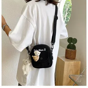 Close-up of black canvas crossbody bag with cute plush bears and adjustable strap