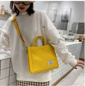 Close-up of bright yellow corduroy crossbody bag featuring a woven label and strap detail