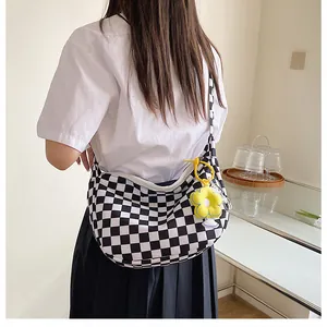 Detail der karierten Canvas-Schultertasche mit gelbem Blumenanhänger an einem Modell