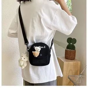 Detail of a black canvas crossbody bag with cute bear patches and a plush pendant