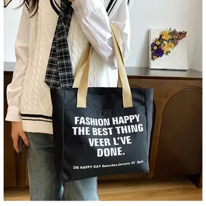 Detail of a black canvas tote bag showing the front pocket and white artistic lettering