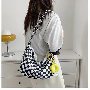 Detail der karierten Canvas-Tasche mit einem leuchtend gelben Gänseblümchen-Anhänger