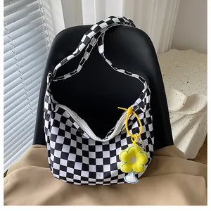 Detail der schwarz-weiß karierten Canvas-Tasche mit einem gelben Blumenanhänger und Reißverschluss
