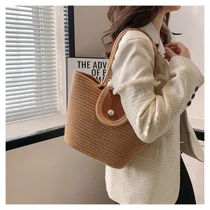 Détail du sac cabas en paille tressée avec rabat en cuir brun et grosse perle