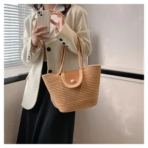 Détail d'un sac cabas en paille tissé avec rabat en cuir marron et fermoir perle