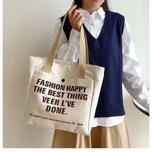 Detail view of cream canvas tote bag with front pocket and dark brown typography