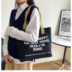 Large black canvas tote bag with beige straps and white typography on a model