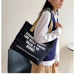 Close-up of a large black canvas tote bag with beige straps carried by a model