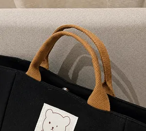 Detail of black canvas bucket bag featuring woven brown handle and metal snap button
