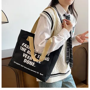 Close-up of a large black canvas tote bag with bold white text and beige shoulder straps