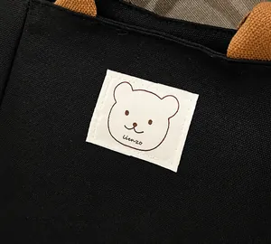 Detail of black canvas bucket bag featuring a cute bear patch and brown woven handle