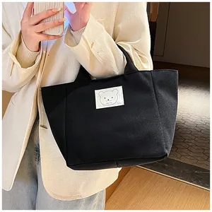 Detailed side view of the black canvas tote bag with a minimalist bear patch on a model