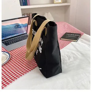 Macro side view of a large black canvas tote bag with beige wide handles and printed text