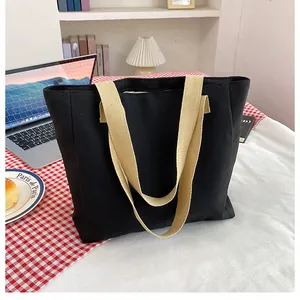 Detail of a large black canvas tote bag with beige woven straps in a lifestyle setting