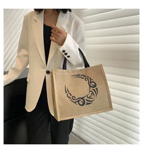 Bolso tote de yute con estampado de luna negra llevado por modelo con blazer blanco