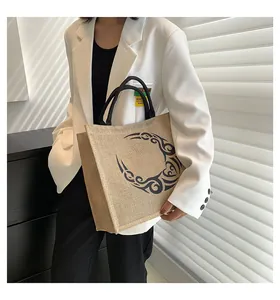 Detalle de bolso tote de yute con estampado de luna y asas negras llevado por modelo