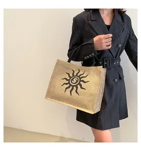 Detalle de bolso tote de yute con espiral solar negra sostenido por modelo elegante