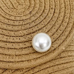 Gros plan sur la texture en paille tressée et la grande perle blanche décorative du sac