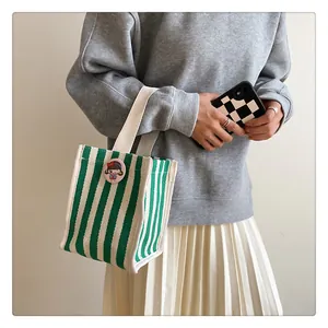 Close-up of green and white striped canvas mini bag with cartoon badge and webbed handles